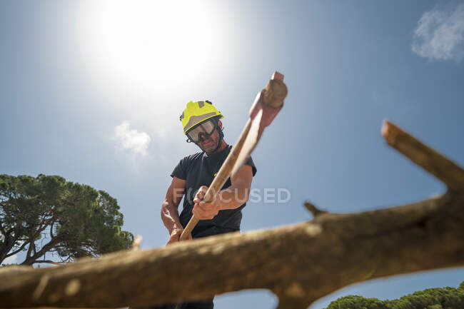 De dessous de pompier en uniforme de protection branche de coupe avec hache en bois sur fond de ciel bleu — Photo de stock