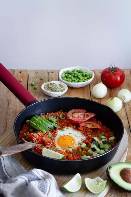 Sabroso shakshuka con huevos y quinua puestos en la mesa con ingredientes frescos - foto de stock