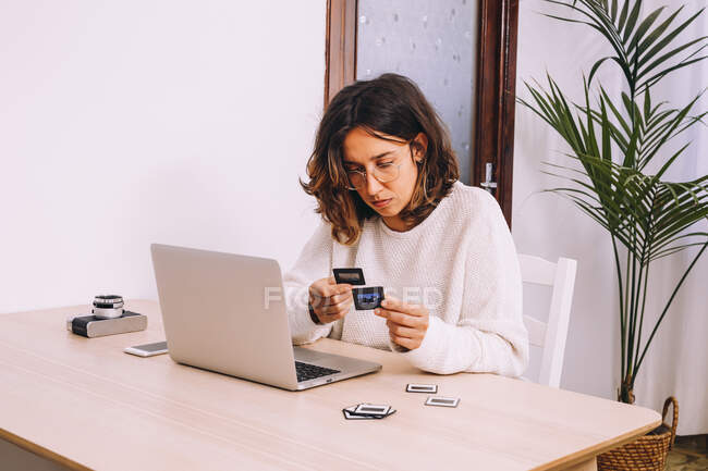 Young female photographer sitting at table with laptop and photo camera with projector and working with old photo slides at home workplace — Stock Photo