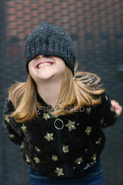 Engraçado criança anônima em casaco quente e tampa de malha cobrindo metade do rosto em pé ao ar livre e sorrindo — Fotografia de Stock