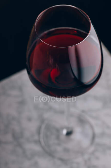 Cristal de vidro clássico de vinho tinto colocado na mesa de mármore sobre fundo preto — Fotografia de Stock