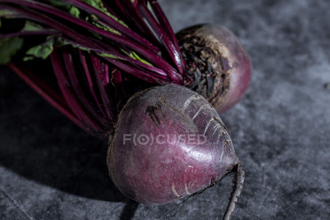 Ganze reife violette Rote Bete mit frischen grünen Blättern auf grau getupftem Tisch — Stockfoto