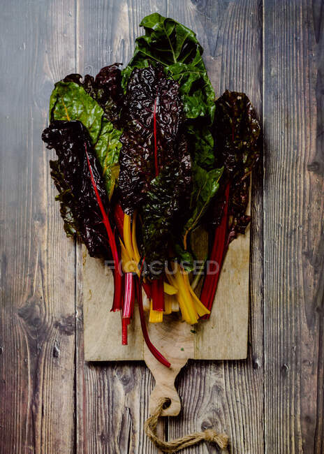 Mazzo di vivido fogliame fresco varicolore di erbe e verdure commestibili su tagliere in legno posto su vecchio tavolo rustico — Foto stock