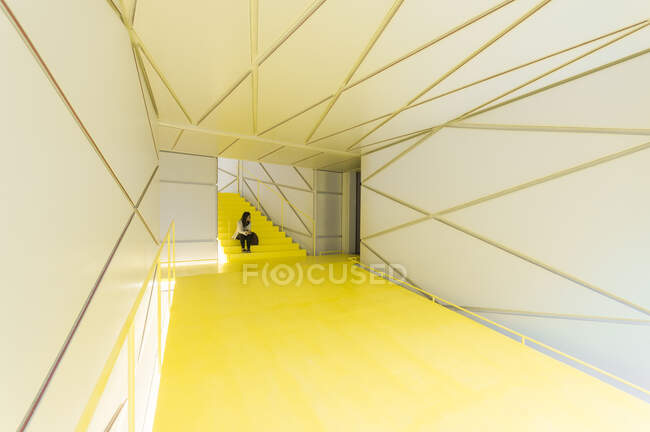 Donna in abbigliamento casual seduta in futuristico corridoio scale gialle con pareti geometriche e soffitto — Foto stock