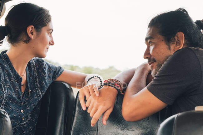 Vista lateral do casal multiétnico sentado olhando um para o outro em automóvel e desfrutando de safári durante as férias de verão — Fotografia de Stock