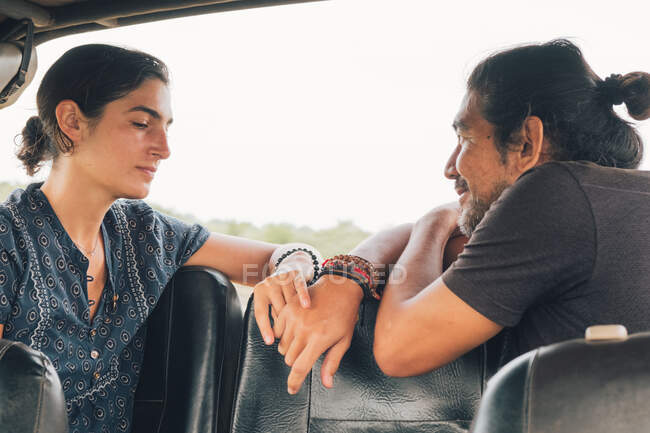 Vista lateral do casal multiétnico sentado olhando um para o outro em automóvel e desfrutando de safári durante as férias de verão — Fotografia de Stock