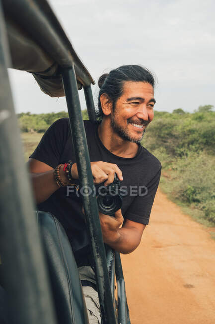 Joyeux voyageur masculin avec appareil photo professionnel prenant des photos de la faune pendant le safari — Photo de stock