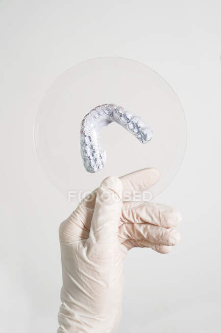 Crop anonymous dentist in medical gloves holding dental prosthesis in modern laboratory — Stock Photo
