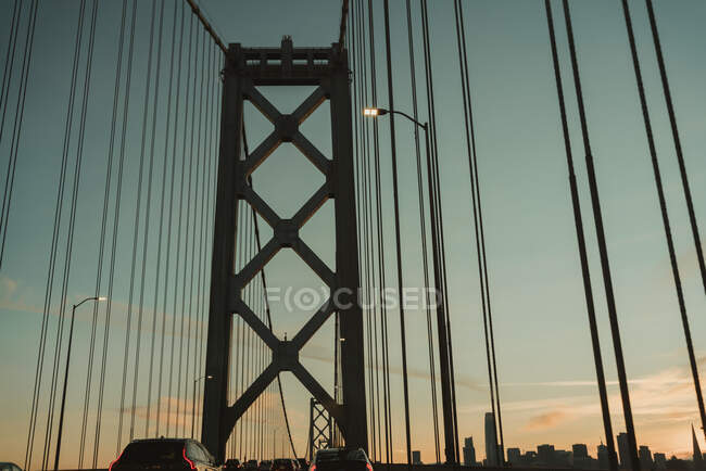 Famous suspension Bay Bridge in San Francisco with moving cars against cloudy sky during sunrise — Stock Photo