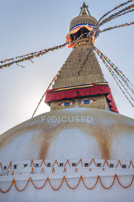 Низкий угол старого буддийского полушария с орнаментом и декоративными глазами на башне с маленьким куполом и гирляндами на вершине под небом во второй половине дня — стоковое фото