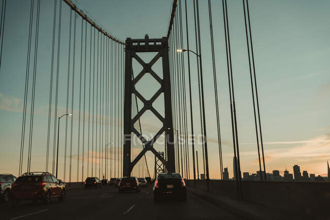 Famoso puente colgante de la bahía en San Francisco con coches en movimiento contra el cielo nublado durante la salida del sol - foto de stock