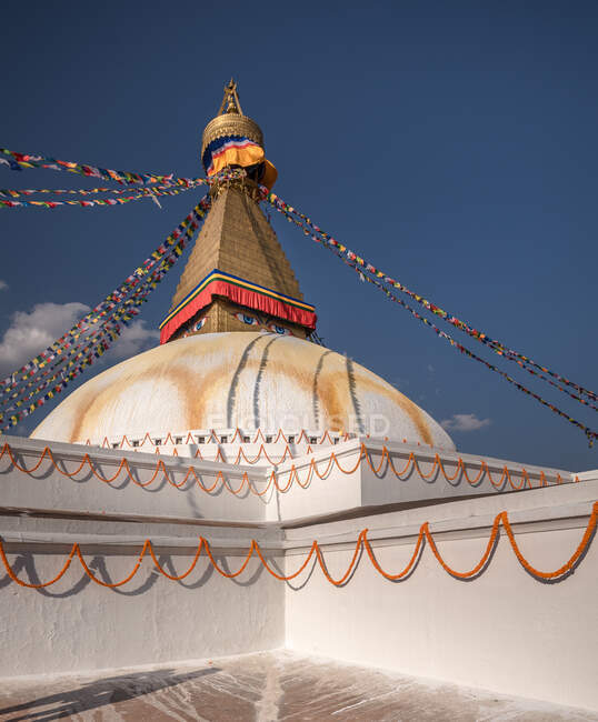 Baixo ângulo do antigo monumento hemisférico budista com ornamento e olhos decorativos na torre com pequena cúpula e guirlandas no topo sob o céu à tarde — Fotografia de Stock