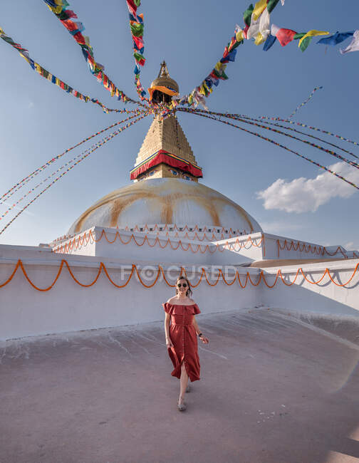 Glückliche Frau blickt in die Kamera, die in der Nähe des buddhistischen Tempels steht, mit dekorativen Girlanden und Turm unter wolkenverhangenem Himmel bei Tageslicht — Stockfoto