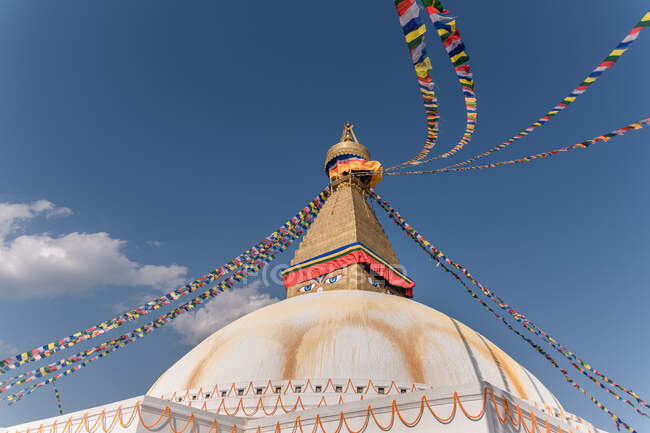 Низький кут старої буддійської півкулі з орнаментом і декоративними очима на вежі з невеликою куполою і садами на вершині під небом вдень. — стокове фото