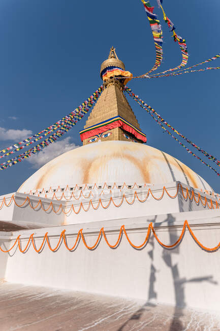 Bajo ángulo del antiguo monumento hemisférico budista con adornos y ojos decorativos en la torre con pequeña cúpula y guirnaldas en la parte superior bajo el cielo por la tarde - foto de stock