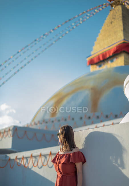 Vista laterale della donna in piedi vicino al tempio buddista con ghirlande decorative e torre sotto il cielo nuvoloso alla luce del giorno — Foto stock