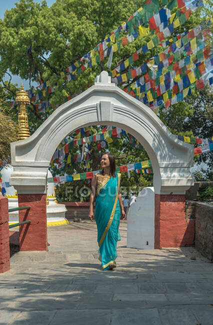 Женщина турист в платье глядя в сторону, стоя на тротуаре ходить по старому буддийскому храму под красочные гирлянды с флагами в солнечный день — стоковое фото