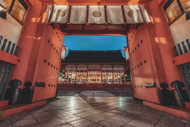 Baixo ângulo de santuário religioso com portões torii e paredes de madeira vermelha em Kyoto à noite — Fotografia de Stock