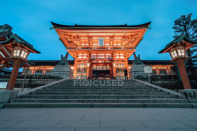 Angle bas de l'extérieur du sanctuaire Fushimi Inari avec fenêtres éclairées et escaliers en pierre le soir — Photo de stock