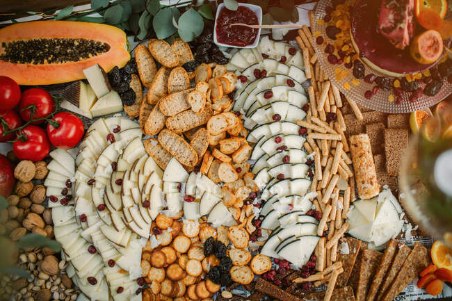 Vue de dessus des fromages et craquelins assortis placés sur la table avec pâtisserie et fruits frais — Photo de stock