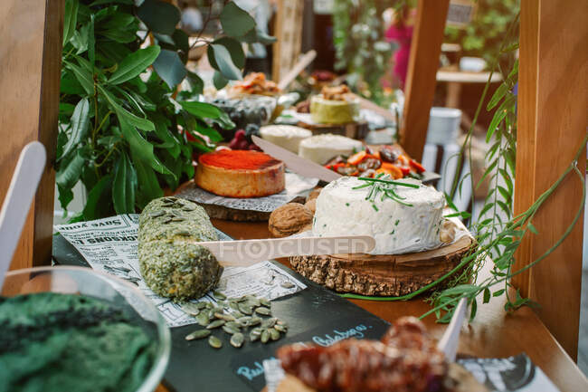 Cottage guarnito con verde e gustoso pane con semi di zucca posto su tavolo di legno vicino a piatti assortiti — Foto stock