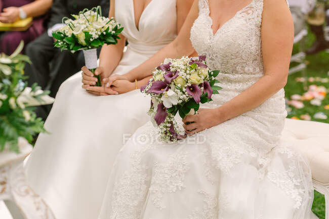 Ernte frisch vermählte homosexuelle Paar in eleganten Brautkleidern sitzen mit zarten Sträußen während des Hochzeitstages — Stockfoto
