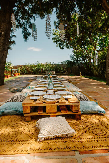 Terrazza estiva con pallet in legno a forma di tavoli e cuscini accoglienti preparati per la celebrazione — Foto stock