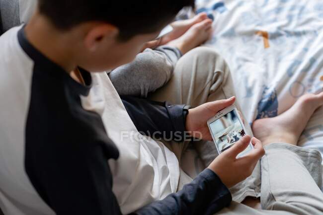 From above of faceless brothers sitting on cozy bed and watching cartoons on cellphones while relaxing at home — Stock Photo