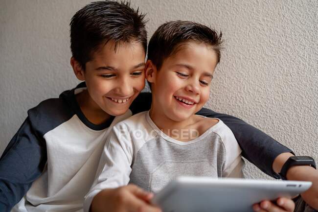 Sorridenti fratelli in pigiama party seduti su un letto accogliente e guardare film insieme mentre si divertono a casa — Foto stock