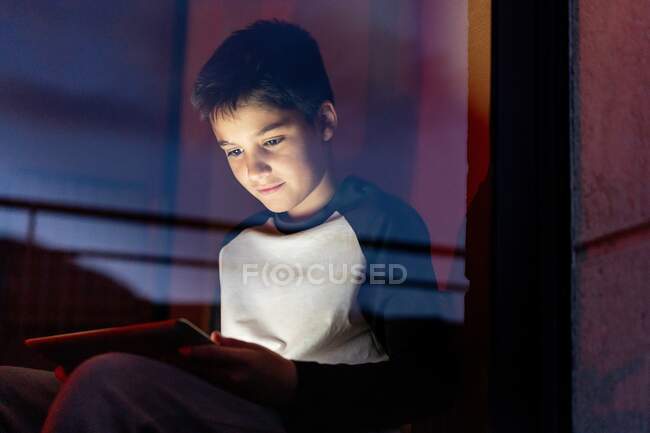 Kid in casual wear playing games on tablet while entertaining during weekend in apartment — Stock Photo