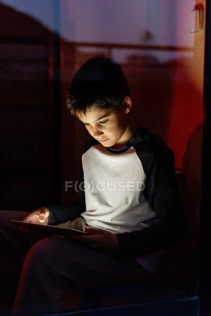 Kid em casual wear jogar jogos em tablet enquanto entretendo durante o fim de semana no apartamento — Fotografia de Stock