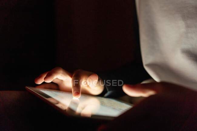 Anonymous crop kid in casual wear playing games on tablet while entertaining during weekend in apartment — Stock Photo