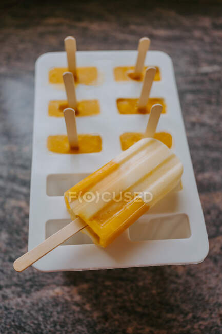 Alto ángulo de delicioso helado en palos colocados en moldes sobre mesa de mármol - foto de stock