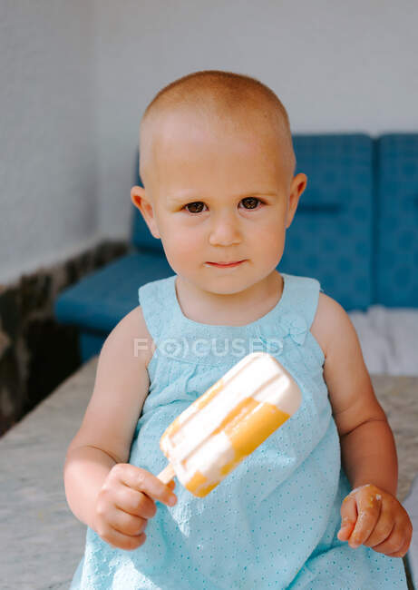Criança bonito sentado em cadeira alta no terraço e comer deliciosos picolés enquanto olha para a câmera — Fotografia de Stock