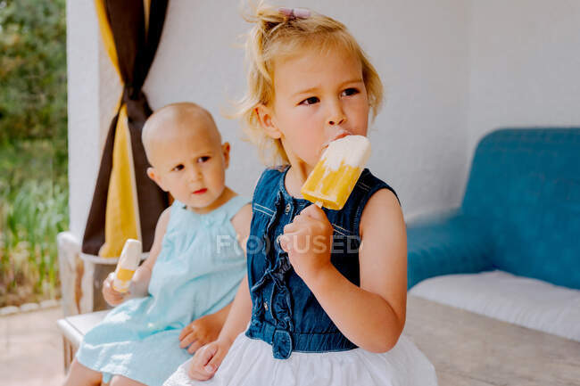Meninas bonitos comendo deliciosos picolés enquanto desfrutam de verão e sentados juntos no quintal — Fotografia de Stock