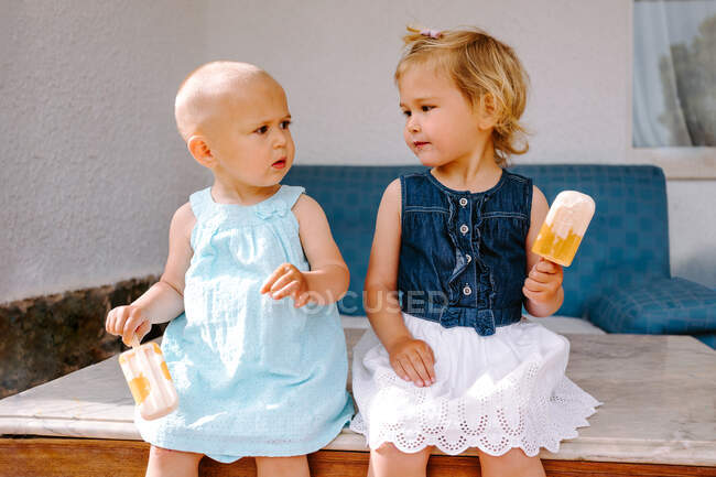 Cute little girls eating yummy popsicles while enjoying summer and sitting together in backyard — Stock Photo