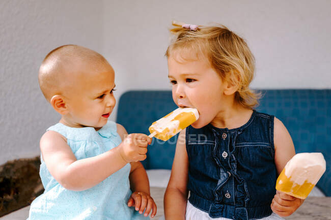Милые маленькие девочки едят вкусное мороженое, наслаждаясь летом и сидя вместе на заднем дворе — стоковое фото
