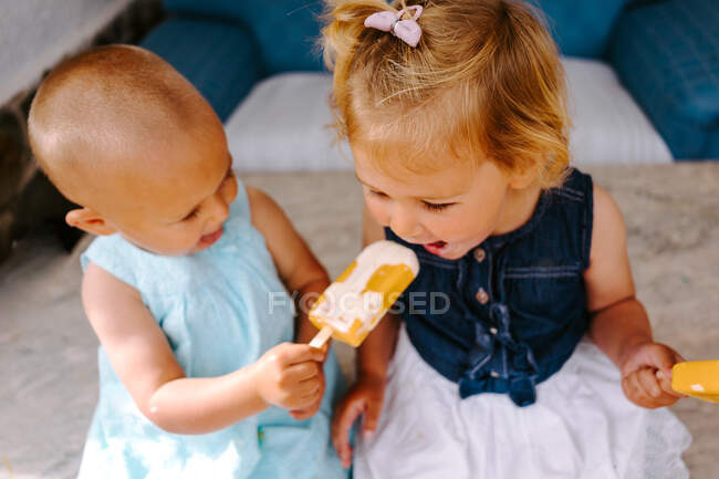 Petites filles mignonnes mangeant délicieux popsicles tout en profitant de l'été et assis ensemble dans la cour arrière — Photo de stock