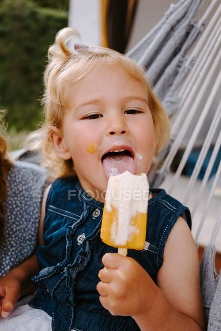 Contenuto bambino che mangia ghiacciolo fatto in casa su bastone mentre si rilassa sulla terrazza in estate guardando altrove — Foto stock