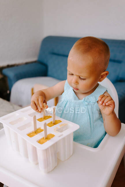 High angle of cute toddler sitting on high chair on terrace and eating delicious popsicles — Stock Photo