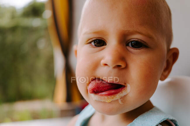 Симпатична маленька дитина дивиться на камеру з брудним ротом насолоджуючись смачним домашнім віскі під час відпочинку на терасі — стокове фото