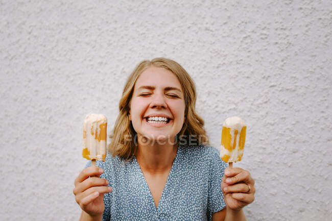 Femme avec les yeux fermés faire drôle grimace visages avec sucettes de glace savoureux sur bâtons sur fond blanc — Photo de stock