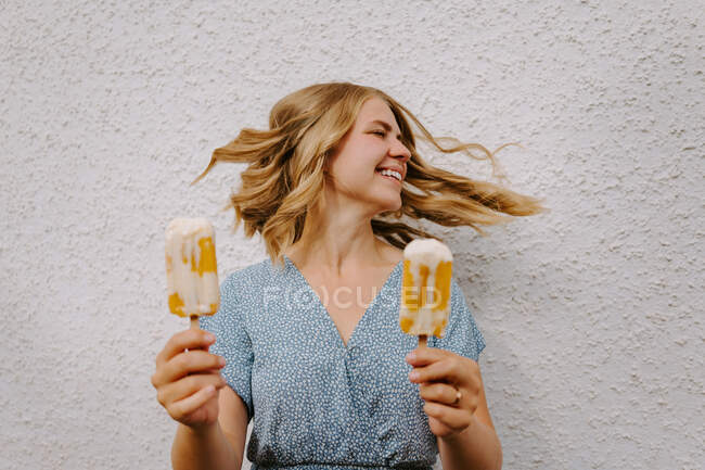 Femme avec les yeux fermés faire drôle grimace visages avec sucettes de glace savoureux sur bâtons sur fond blanc — Photo de stock