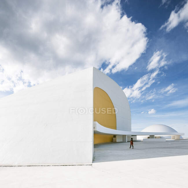 Exterior do edifício de auditório com paredes curvas brancas e amarelas localizadas na praça de concreto branco do Centro Cultural Internacional Oscar Niemeyer contra o céu azul nublado em dia ensolarado na Espanha — Fotografia de Stock
