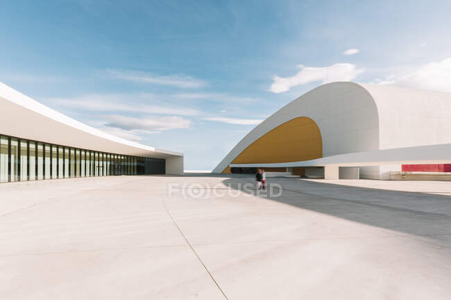 Esterno dell'edificio dell'auditorium con pareti curve bianche e gialle situato sulla piazza di cemento bianco del Centro Culturale Internazionale Oscar Niemeyer contro il cielo blu nuvoloso nella giornata di sole in Spagna — Foto stock