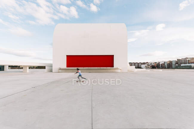 Personne anonyme à cheval skateboard sur la place pavée près du bâtiment auditorium moderne du Centre culturel international Oscar Niemeyer en Espagne — Photo de stock