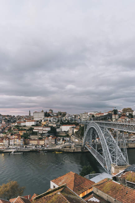 Drone view of amazing cityscape with bridge over calm river and residential houses under cloudy sky — Stock Photo