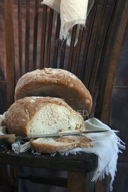 Laibe leckeres Brot und scharfes Messer auf einem Stück Stoff auf einem Holzstuhl — Stockfoto