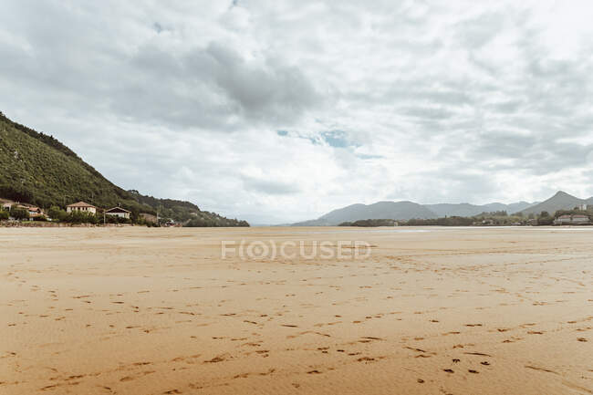 Calm sandy coast during low tide and green hills with buildings — Stock Photo