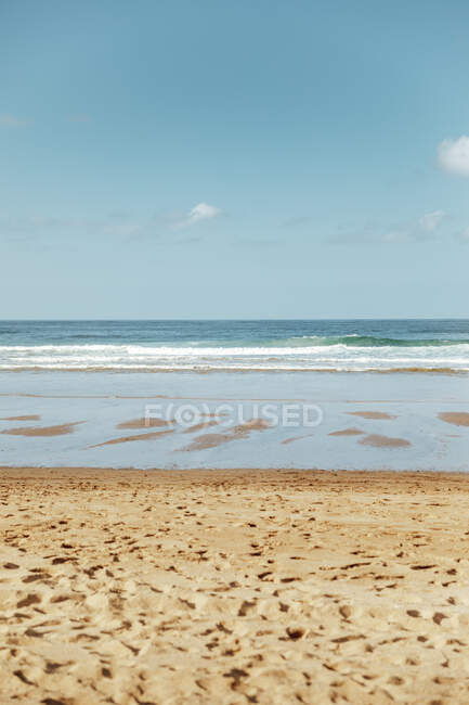 Піщаний пляж з океанськими хвилями і блакитним хмарним небом. — стокове фото